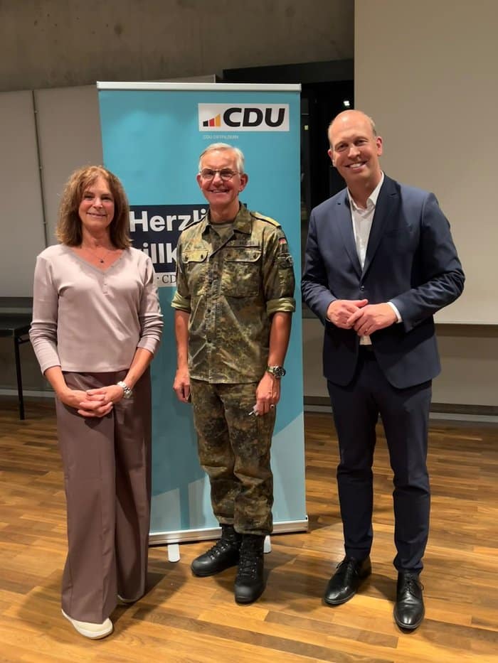 Kapitän zur See Michael Giss (Mitte) mit zwei Gastgebern vor einem Banner der CDU Ostfildern