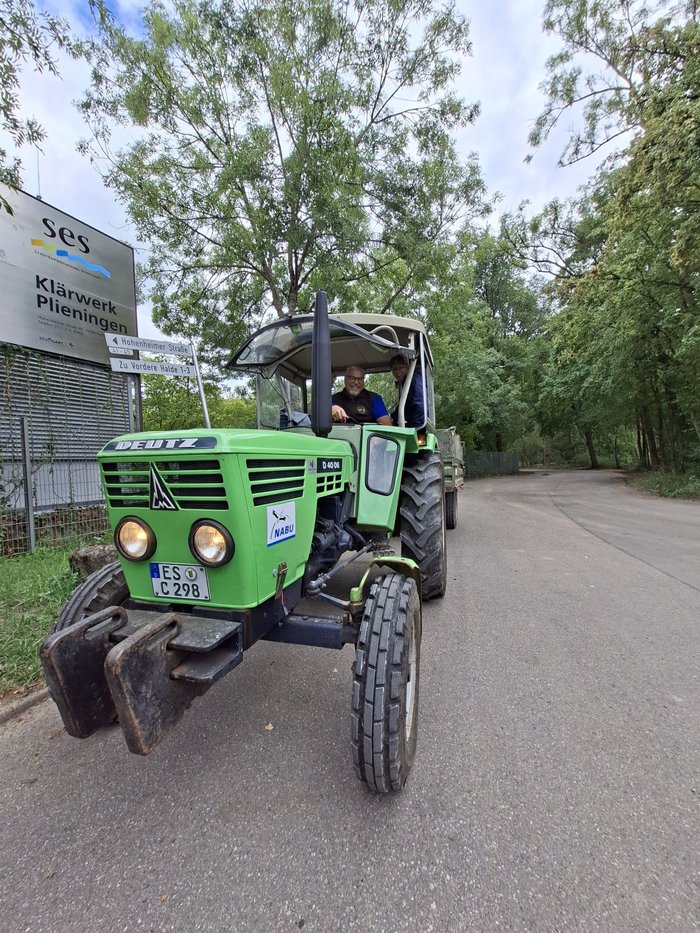 Grüner Traktor mit Anhänger und NABU-Aufkleber transportiert die Ausrüstung