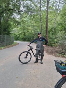 NABU-Aktiver in Wathose und Fahrradhelm neben seinem Mountainbike auf einem Weg im Grünen