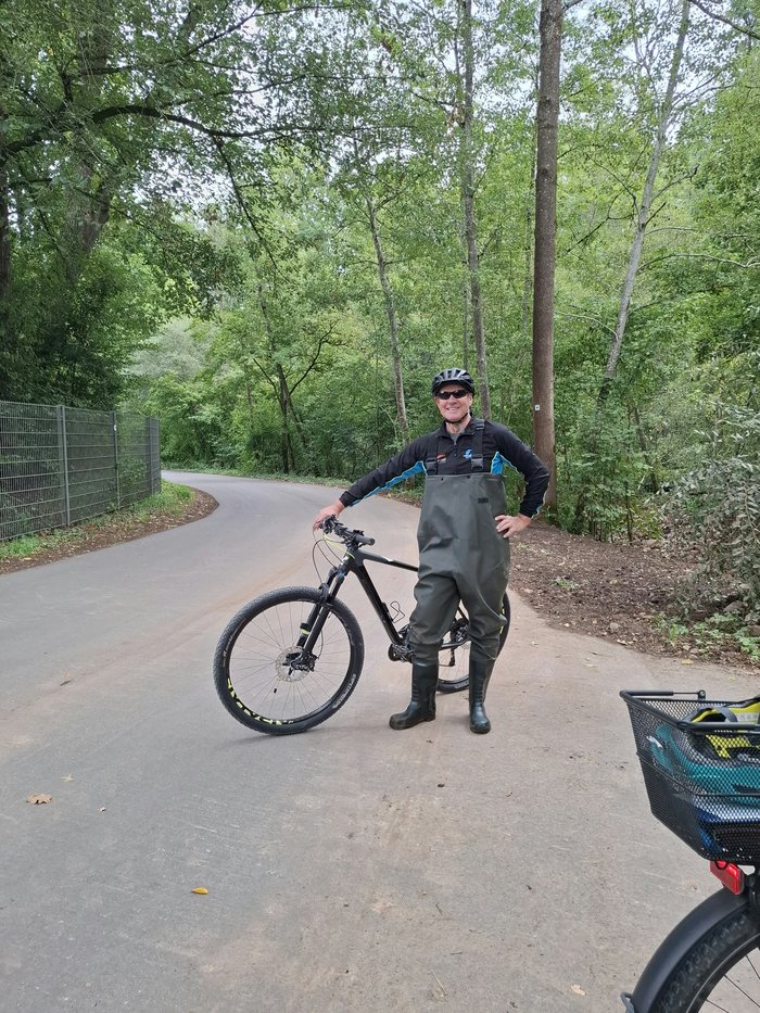 NABU-Aktiver in Wathose und Fahrradhelm neben seinem Mountainbike auf einem Weg im Grünen